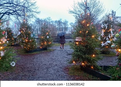 Lonely Woman Walking In The Park With Umbrella Among Decorated Christmas Trees. Climate Change Proof, No Snow December, Global Warming Consequences