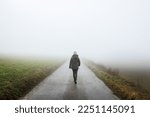 Lonely woman walks on empty road in fog. Journey to unknown place. Solitude female person walking outdoors
