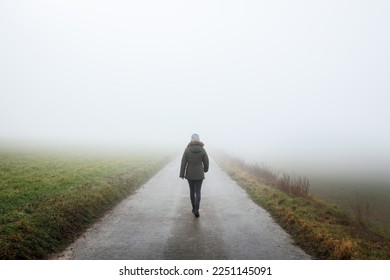 Lonely woman walks on empty road in fog. Journey to unknown place. Solitude female person walking outdoors