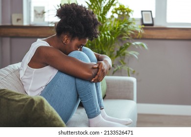 Lonely young African American woman sitting on bed. Depressed girl at home, looking away with sad expression. Upset Afro Girl Sitting On Couch With Cellphone, Thinking About Something - Powered by Shutterstock