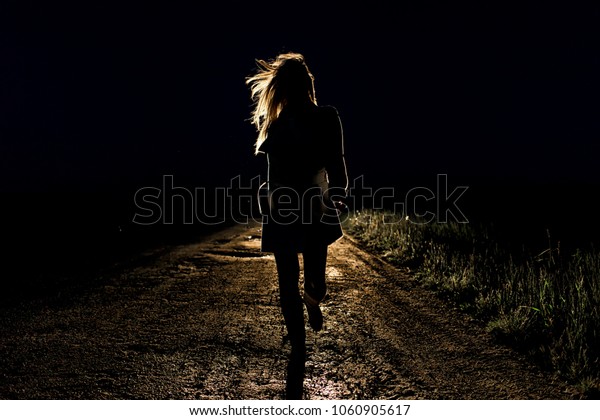 lonely young\
frightened woman on an empty night road runs away in the light of\
the headlights of her\
car