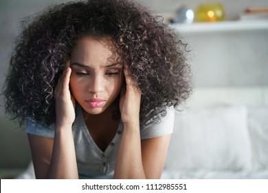 Lonely young latina woman sitting on bed. Depressed hispanic girl at home, looking away with sad expression.