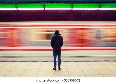 Einsamer junger Mann, der von hinten in der U-Bahn-Station mit unscharfem, sich bewegender Zug auf dem Hintergrund erschossen wurde