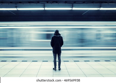 Lonely young man shot from behind at subway station with blurry moving train in background