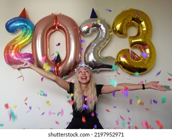 Lonely Young Woman Celebrating New Year 2023 At Home. Smiling Girl With Hands Up. Big Colorful Number Balloons.silvester Party. December 31.party Decoration. Confetti Falling. January 1.flower Wreath