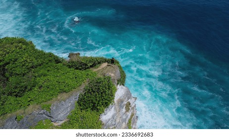 A lonely young woman stands on the edge of a cliff in a black dress. Bird's eye view of the cliff and a young woman standing and looking out over the ocean. Turquoise ocean water and foam from waves. - Powered by Shutterstock