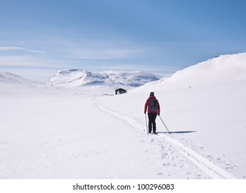 Lonesome female skier approaching a small cottage in norwegian mountains at easter