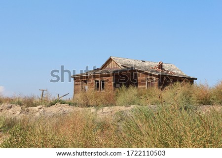 A long abandoned farm house on the Front Range of Colorado.  Weathered wooden boards, broken windows, dilapidated shingles and a crumbling brick chimney with a blue sky and grassy foreground.