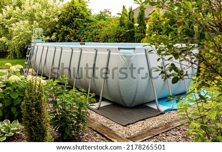 Long, above ground, rectangular, rack (frame) swimming pool outdoor in the garden. Summer holiday (vacation) and recreation.