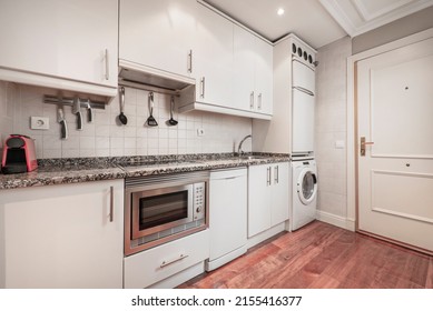 Long Apartment Kitchen With White Cabinets, Pink Granite Countertops, Built-in Appliances, And Brownwood Parquet Flooring