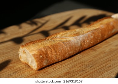 Long Baguette On Wooden Chopping Board With Shadows