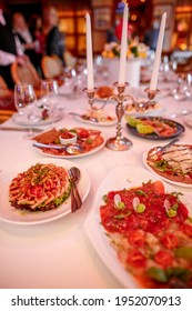 Long Banquet Table With Candles And Delicious Meals On White Plates.