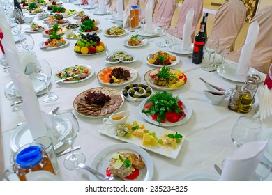 Long Banquet Table. On The Table, Drinks And Snacks. A Table Covered With A White Tablecloth. Around There Are Chairs In The Covers.