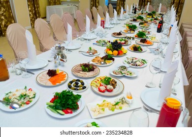 Long Banquet Table. On The Table, Drinks And Snacks. A Table Covered With A White Tablecloth. Around There Are Chairs In The Covers.