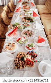Long banquet table set with assorted appetizers, salads, glassware and red folded napkins—an elegant party spread for celebrations, family gatherings, weddings or festive holiday dinners.