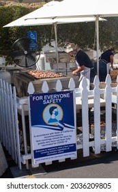 Long Beach, CA - September 4 2021:  Greek Festival In Long Beach Open Again During Covid.  A Man Grills Lamb Chops Behind A Covid  Warning Sign. 