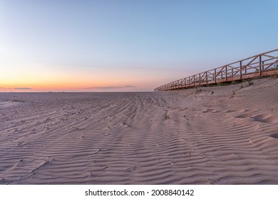 Long beach of fine sand undulating in the wind, with a wooden walkway, in the light of dawn. - Powered by Shutterstock