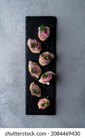 Long Black Stone Platter Filler With Herring And Potato Gourmet Canape, Elegant And Fancy Menu Photo On Grey Concrete Background