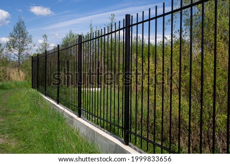 Long black transparent metal fence with concrete foundation against blue sky. Diagonal arrangement.