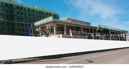 Long blank hoarding with white canvas mounted on construction site with unfinished building with wall and scaffold - Shutterstock ID 2194239927
