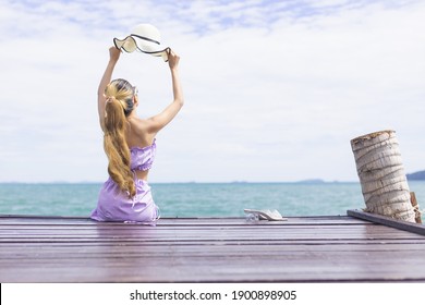 Long Blown Hair Woman Wearing Blue Dress Sit On The Bridge Lift Up The Hat Looking At The Sea