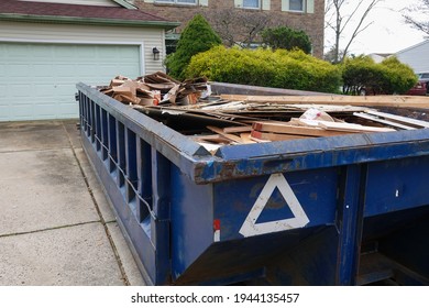 Long blue dumpster full of wood and other debris in the driveway in front of a house in the suburbs