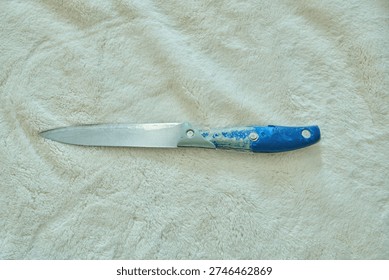 Long blue-handled knife lying flat on a soft beige towel, single subject, clean product-style shot