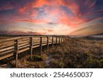 a long brown wooden footpath to a sandy because with a gorgeous sunrise, ocean water and waves in Carolina Beach North Carolina USA