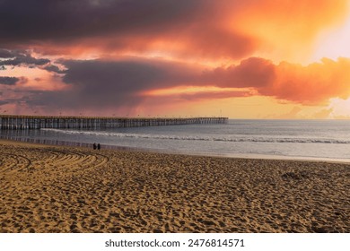 a long brown wooden pier with American flags flying on curved light posts with people walking and fishing on the pier with powerful clouds at sunset at Ventura Pier in Ventura California USA - Powered by Shutterstock