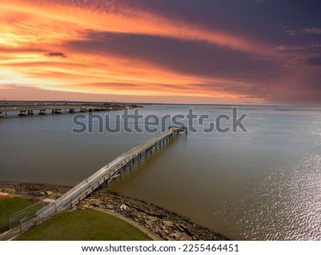 A long brown wooden pier of the rippling waters of Mobile Bay with cars driving on the highway and powerful clouds at sunset at USS Alabama Battleship Memorial Park in Mobile Alabama USA
