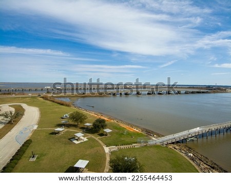 A long brown wooden pier of the rippling waters of Mobile Bay with cars driving on the highway and a gorgeous blue sky with clouds at USS Alabama Battleship Memorial Park in Mobile Alabama USA