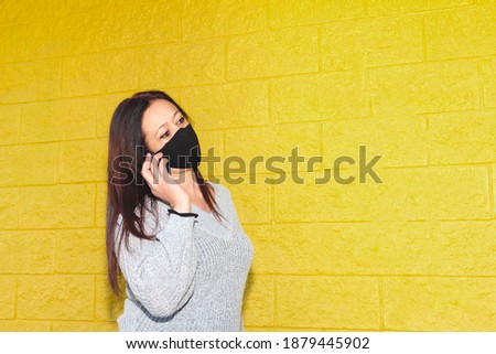 Long brown-haired caucasian woman has a phone conversation with the smartphone on a yellow background. Concept of progress in wireless technology.
