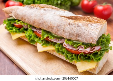Long Ciabatta Sandwich with lettuce, slices of fresh tomatoes, ham, turkey breast and cheese cut in half
