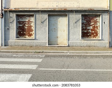 Long closed shop with rusty shutters and store sign removed over the entry. Urban background.