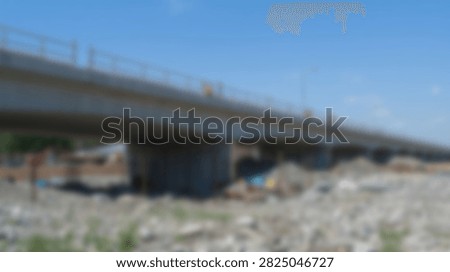 A long concrete bridge with multiple pillars crosses a dry, rocky riverbed. The sky above is clear and blue, indicating a sunny day.