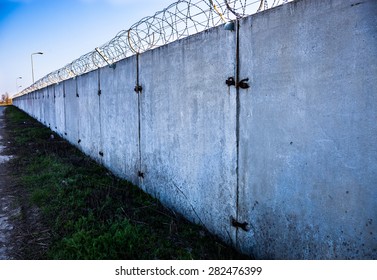 Long Concrete Wall With Barbed Wire On Top.