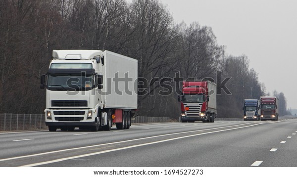 A long\
convoy of lorries on suburban highway road at cloudy spring day,\
goods delivery transportation\
logistics