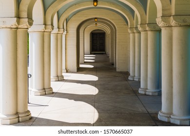 A long corridor in classical architectural style with many beautiful columns leading through arches in perspective to a door