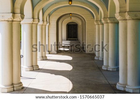 A long corridor in classical architectural style with many beautiful columns leading through arches in perspective to a door