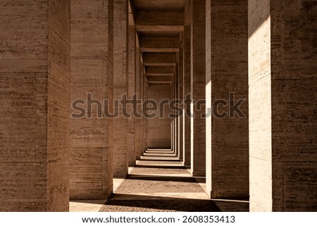Long corridor with stone pillars and dramatic shadows. Strong symmetry and warm light create a minimalist and timeless architectural background