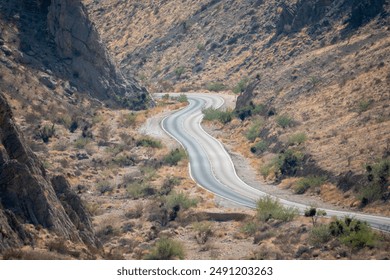 A long, curvy road winds through a desert. The road is empty and the landscape is barren - Powered by Shutterstock