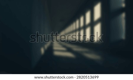 A long, dark corridor with a repeating pattern of windows casting light and shadows.