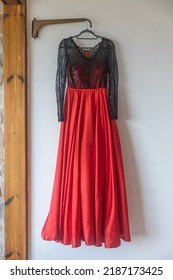 A Long Dark Red And Black Bridesmaid Dress With Embroidery And Sequins Is On A Hanger On The Wall