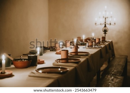A long dining table set for a medieval-style feast in a historic vaulted room. The warm glow of candles creates a cozy and serene ambiance, highlighting rustic tableware and ancient architecture
