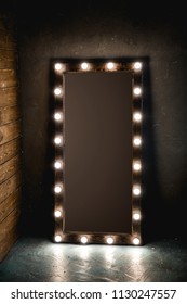 Long dressing mirror with light bulbs stands on the floor against a wooden and concrete wall in loft style room. with brown background. place for text
