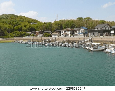 A long embankment of a fishing port and series of fishing boats moored to it.
A landscape of a seaside town and its port.
A view of the coast line of an inland sea in Japan.