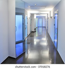 Long, Empty Corridor In A Hospital Or Office Building, With The Ceiling Lights Reflected On The Shiny Floor.