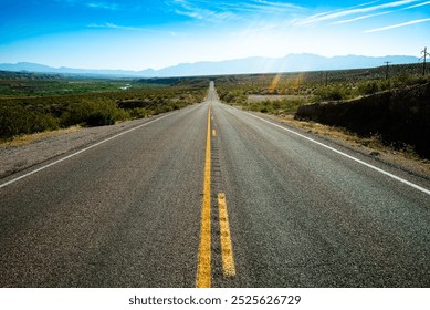 Long, empty desert highway stretches toward distant mountains under a bright blue sky, symbolizing freedom, exploration, and endless adventure on the open road.
 - Powered by Shutterstock