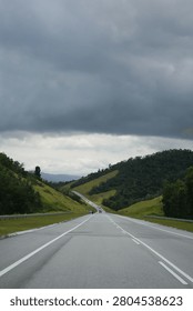 Long empty highway stretching through green rolling hills and lush tropical mountains under a dramatic stormy sky with dark rain clouds