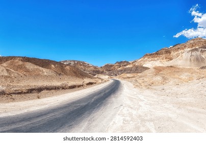 A long, empty highway stretching through the desert landscape of Death Valley, California, with distant mountains and vast blue sky, symbolizing travel, isolation, and the open road in the American West.